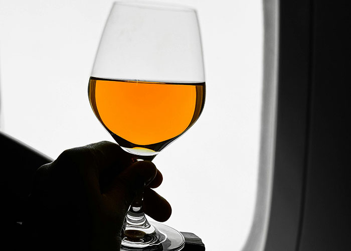 A person holding a glass of orange beverage on a plane next to the window.
