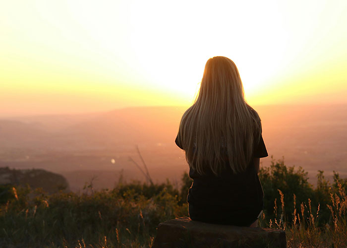 Woman with long hair sitting alone watching sunset, reflecting on heartbroken stories of people who realized cheating in relationships.