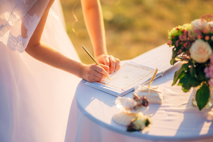 Bride signing wedding certificate at a decorated table in a super normal thing country outdoor ceremony setting.