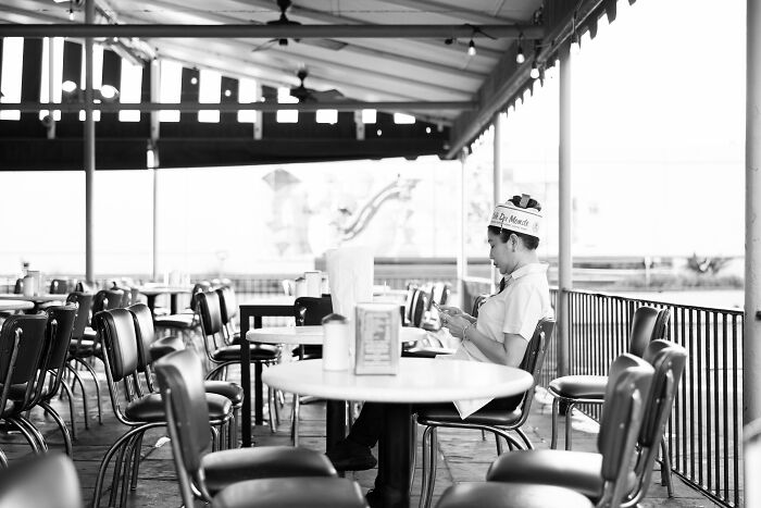 Black and white image of a waiter seated in an empty outdoor café, part of the 2025 World Food Photography Awards.
