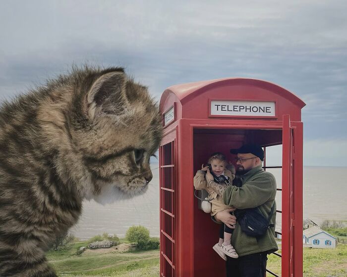 Giant cat photoshopped beside a red phone booth with a man and child inside, creating a surreal world.