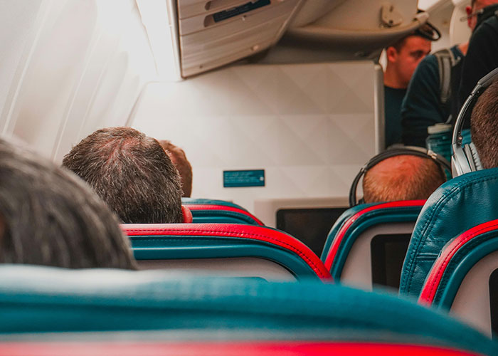Airplane interior with passengers seated, viewed from the back, highlighting onboard experiences.