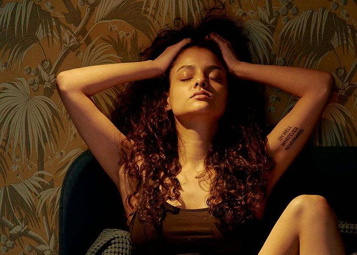 Woman with curly hair sitting with eyes closed, appearing heartbroken, reflecting on cheating in a relationship.