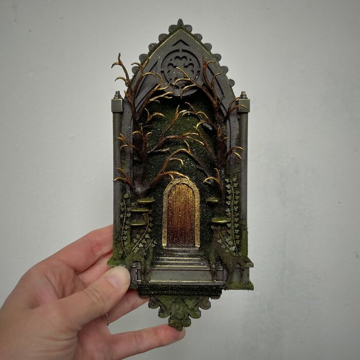 Hand holding an intricately designed diorama with a mysterious golden door and gothic details.