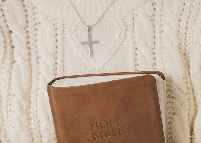 Person wearing a cross necklace and holding a Bible.