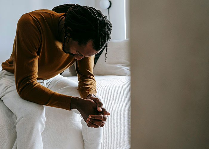 Man sitting on bed with head down, appearing heartbroken, reflecting on cheating in a significant relationship