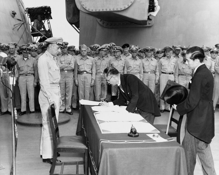 A historic WWII moment captured as a man signs documents surrounded by military officers.