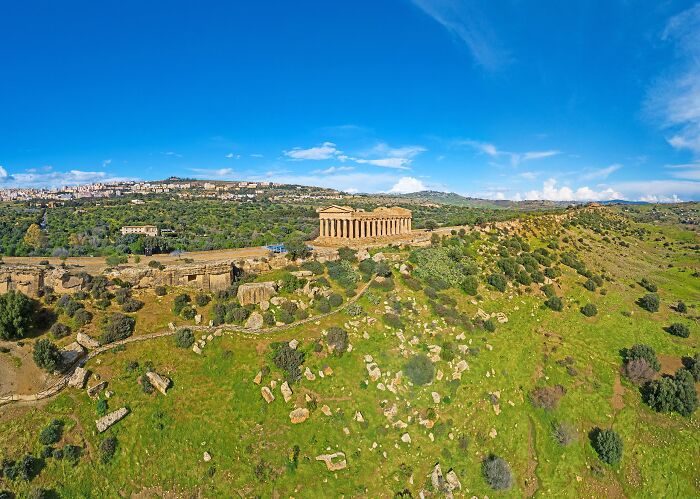 Aerial view of a well-preserved ancient temple set in a lush, green landscape against a bright blue sky, showcasing architectural wonders.