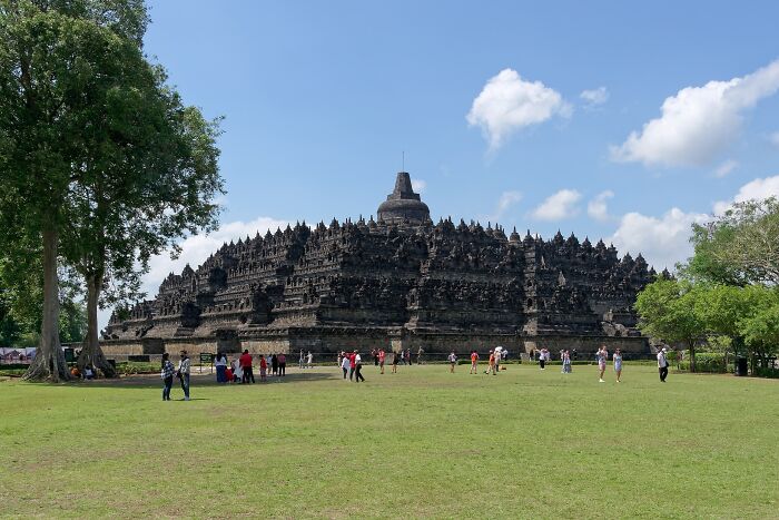 A magnificent, ancient architectural wonder stands under a clear blue sky with visitors exploring the site.