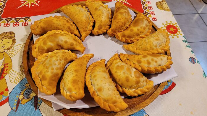 Golden brown empanadas, a popular dish, arranged on a wooden plate on a festive tablecloth.