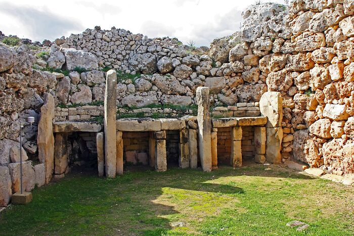 Ancient man-made stone structure with large vertical pillars and a circular surrounding wall under a cloudy sky.