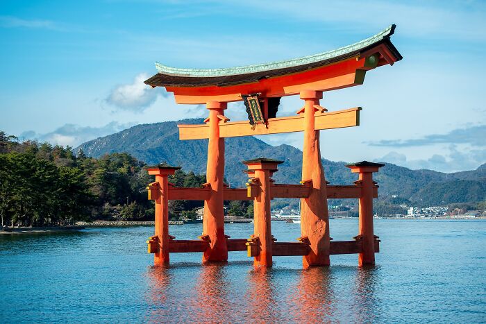 An architectural wonder, a traditional Japanese torii gate stands in the water with mountains in the background.