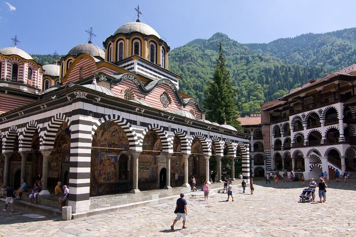 Architectural wonder with striped arches and domes, visitors exploring, surrounded by mountains.