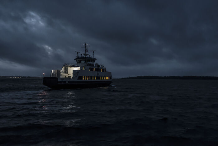 Ferry sailing in dark, ominous waters at night, evoking a sense of fear and solitude.
