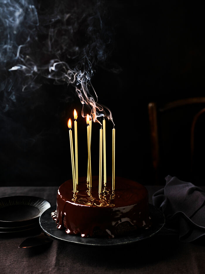 Chocolate cake with tall gold candles, emitting smoke, featured in World Food Photography Awards 2025 shortlist.