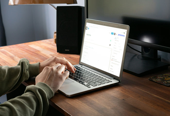 Person typing on a laptop at a wooden desk, engaged in job hunting online.
