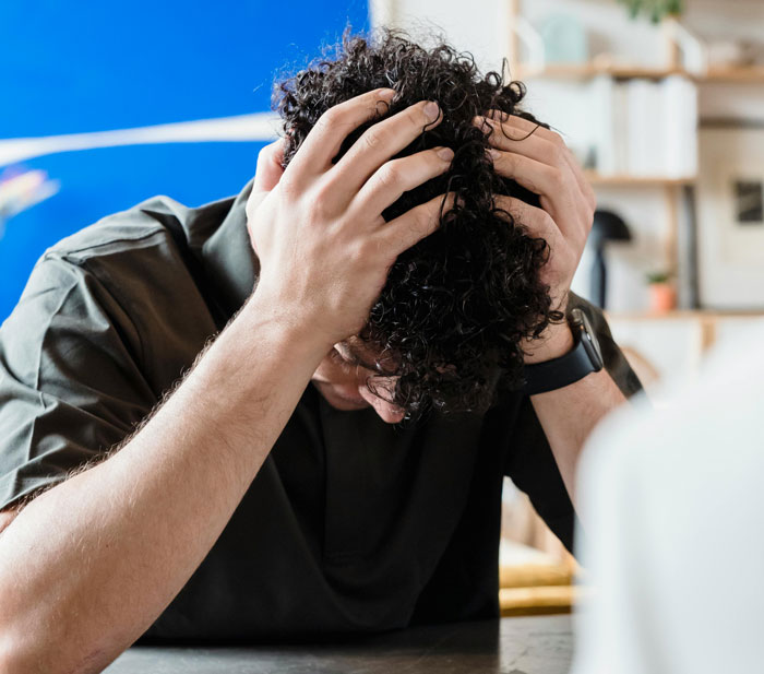 Person with head in hands, illustrating stress from being too close to parents, in a modern room with shelves.