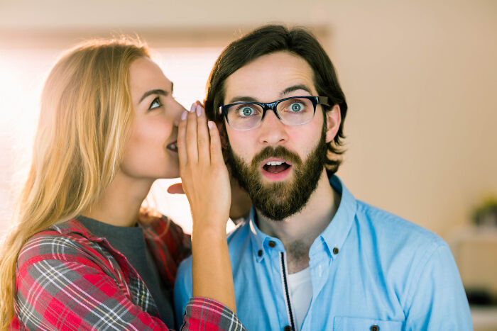 Woman whispers to surprised man in casual attire, illustrating dating insights on men's unique behaviors.