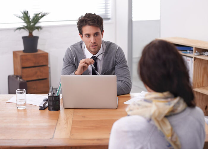 Man in gray sweater conducting job interview with woman, illustrating ridiculous questions asked during job interviews.