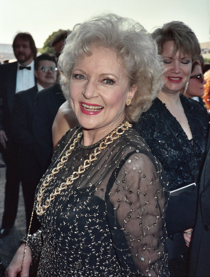 Elderly woman in elegant attire smiling at an event, capturing the essence of beloved stars with warmth and charm.