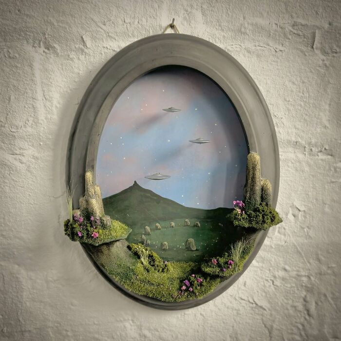 Oval diorama by Caroline Dewison, featuring UFOs in a night sky over a mysterious landscape.