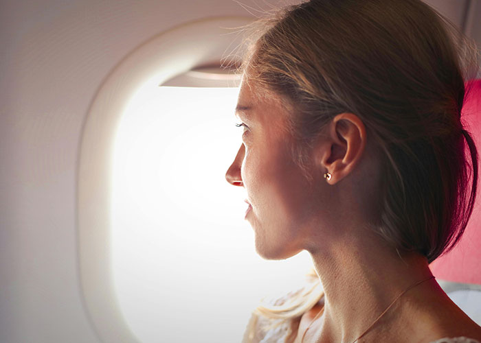 Woman gazes out airplane window, pondering an unbelievable moment mid-flight.