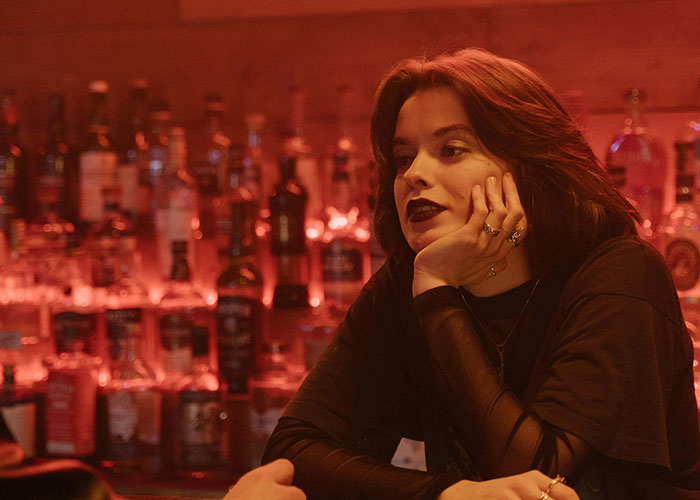 Young woman with dark lipstick sitting at a bar counter, reflecting on heartbreak and signs of cheating in relationships.