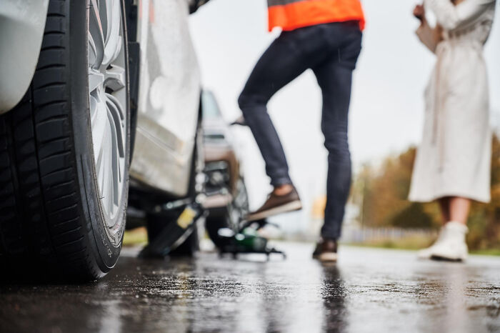 Person in orange vest inspecting car wheel on wet road, highlighting gut instincts for safety.
