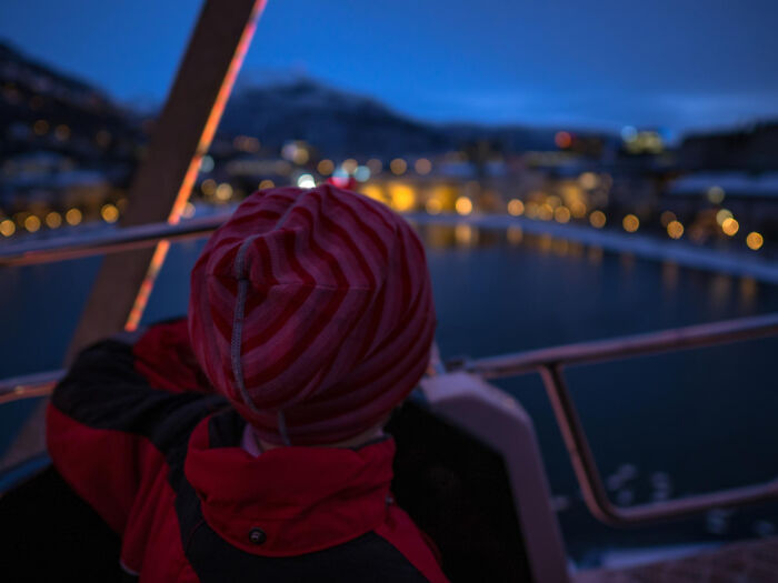 Person in a red jacket and beanie overlooking a lit-up evening cityscape by the water, trusting their gut.