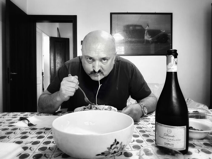 Man eating spaghetti at a dining table with a bottle of wine, featured in the 2025 World Food Photography Awards.