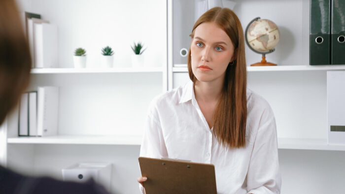 Woman in a white shirt holding a clipboard, listening intently during a job interview with ridiculous questions asked.