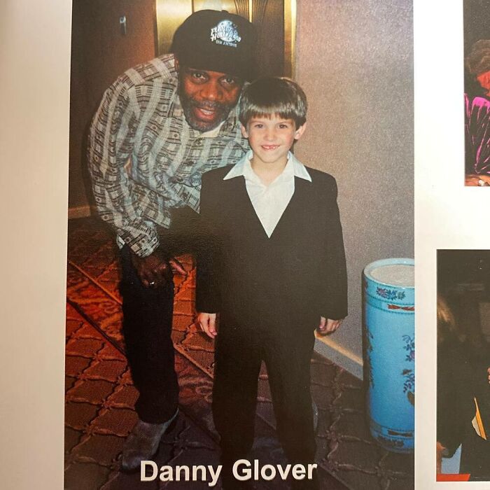 A young boy in a suit taking a photo with a celebrity inside a building, standing on patterned carpet.