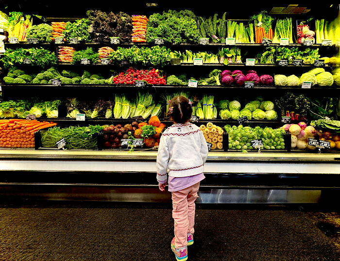 Child admiring vibrant vegetables at a supermarket; World Food Photography Awards 2025 shortlist contender.