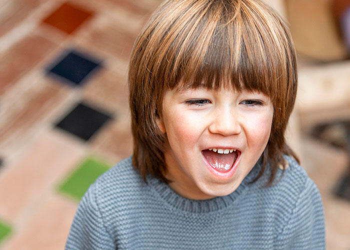 Three-year-old child with a joyful expression, wearing a gray sweater, in a colorful indoor setting.