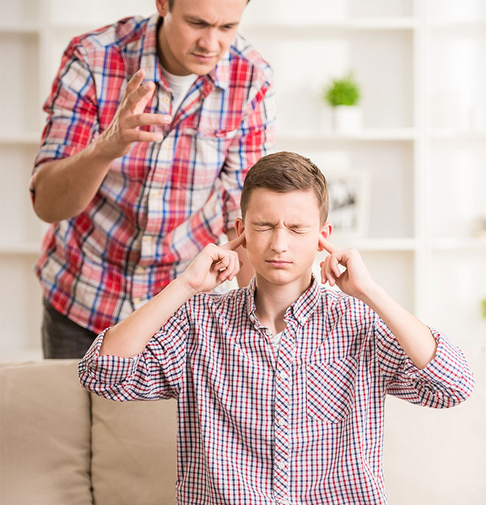 Teen blocks ears as man talks, expressing frustration from years of harassment labeled as a "harmless prank.