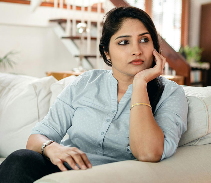 Woman looking concerned and thoughtful on a sofa, reflecting on MIL's baby comment.