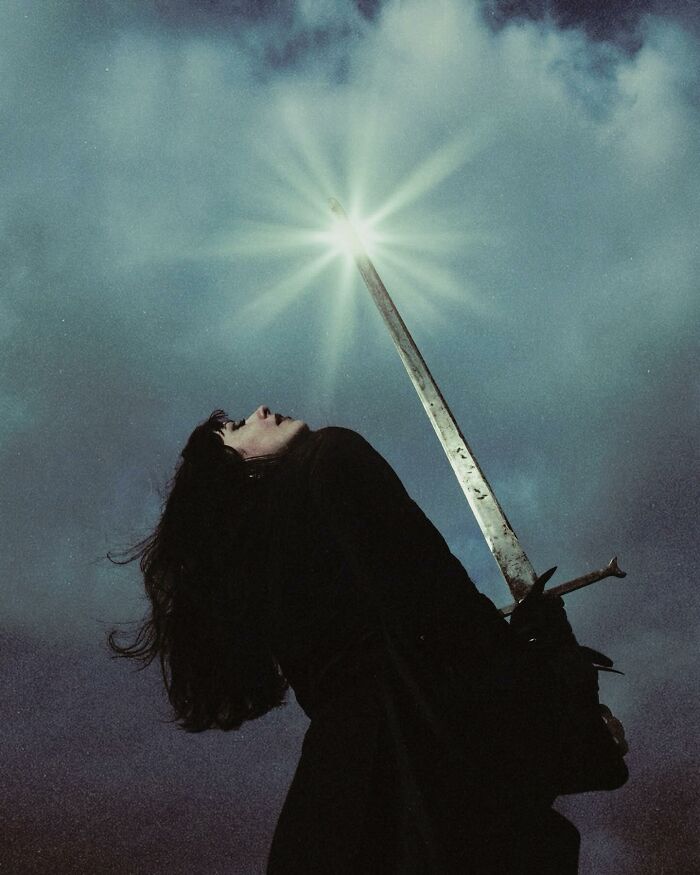 Dark escapism photography by Nona Limmen, featuring a figure holding a glowing sword under a cloudy sky.