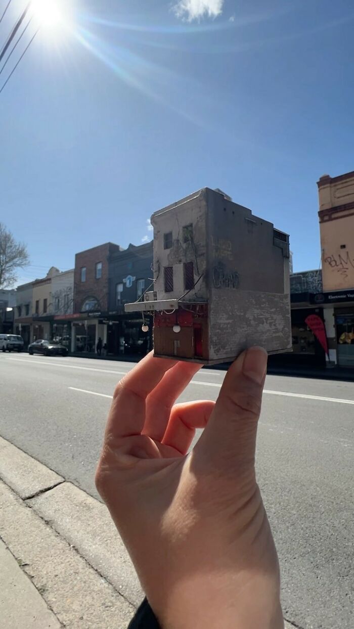 Hand holding a miniature building against a street backdrop, capturing the essence of secret worlds in miniatures.