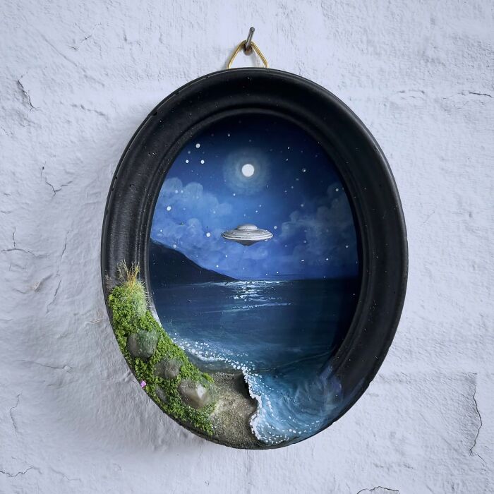 Alien-themed diorama by Caroline Dewison: UFO over a moonlit ocean in an oval frame, with mossy landscape details.