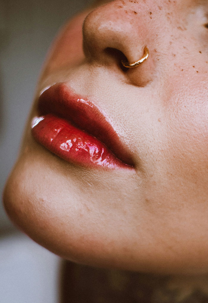 Close-up of a nose with a gold ring and glossy red lips, showcasing unique style for job hunting tips.