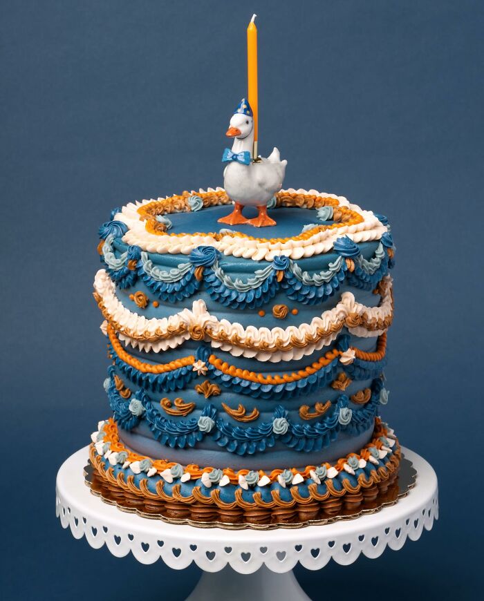 Colorful cake decorated intricately with blue and orange frosting, topped with a duck figurine and candle.