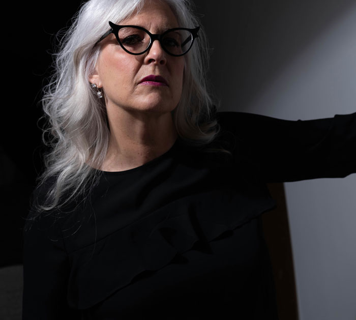 Elderly woman with silver hair and glasses, wearing black, illustrating a story about close parent-child relationships.