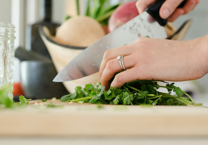 Hands chopping cilantro with a knife on a kitchen board, showcasing everyday life hacks.