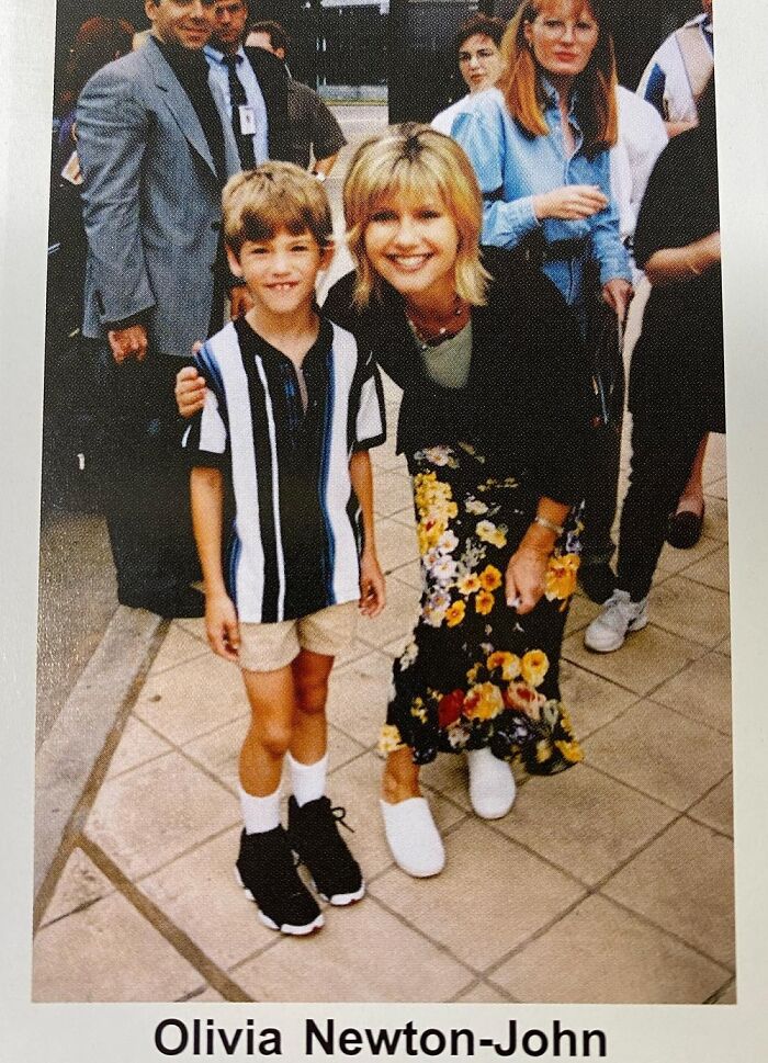 Young boy in striped shirt posing with a well-known celebrity outdoors, surrounded by a crowd.