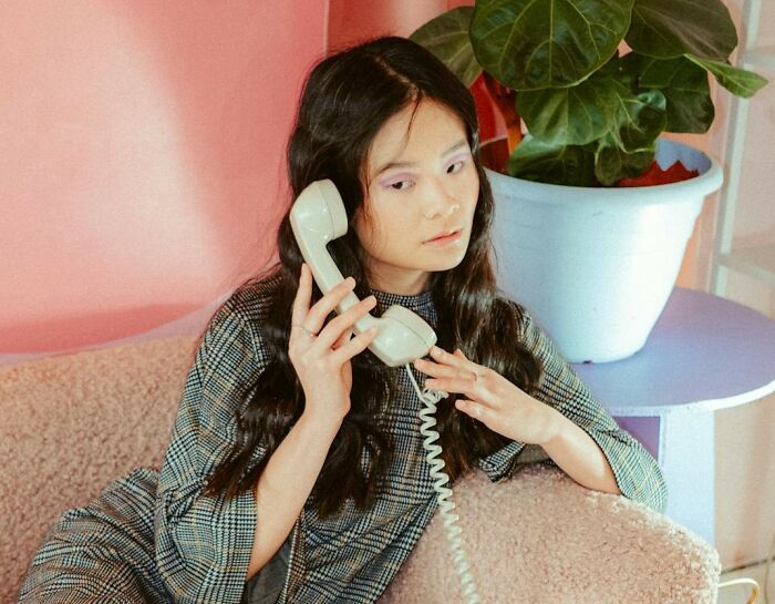 Woman using a vintage phone, sitting in a cozy chair near a plant.