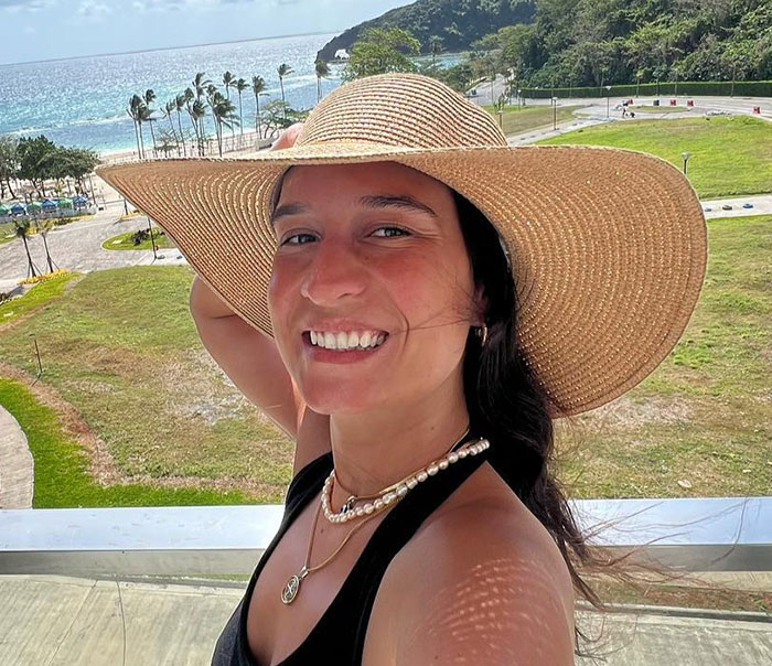 Young woman wearing a sun hat, smiling outdoors by the sea, representing mysterious illness while traveling.