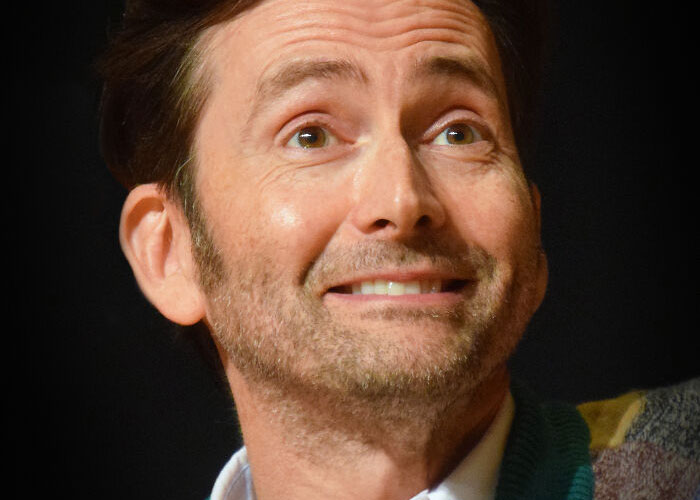 Celebrity smiling warmly, wearing a colorful sweater over a white shirt.