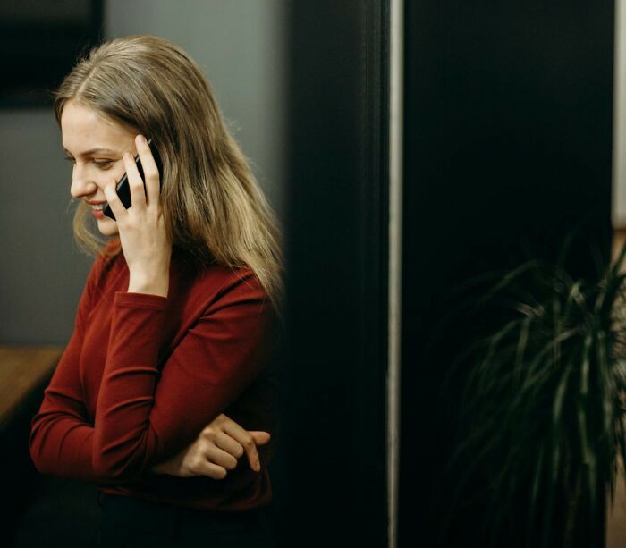 Woman in red shirt on phone, listening to her gut in a thoughtful moment near a plant.