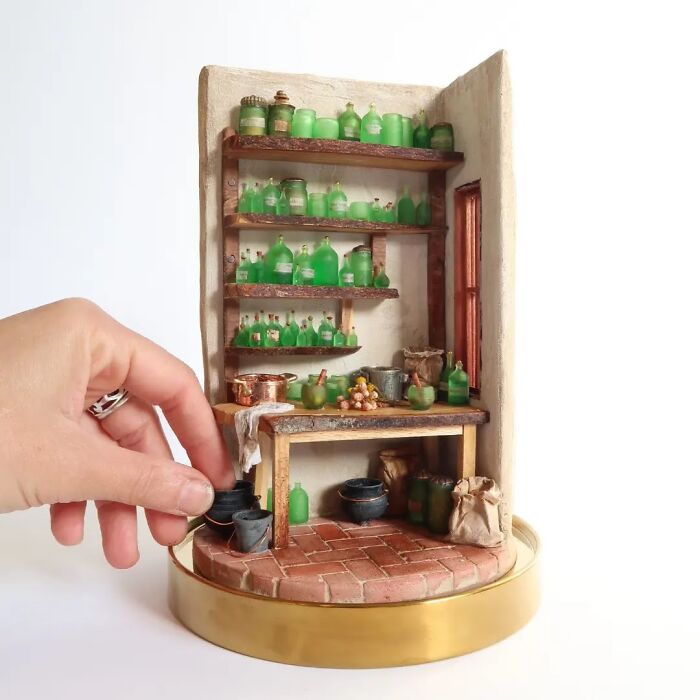 Miniatures by Tamar Cohen, featuring a tiny apothecary shop with green bottles and a hand adjusting items.