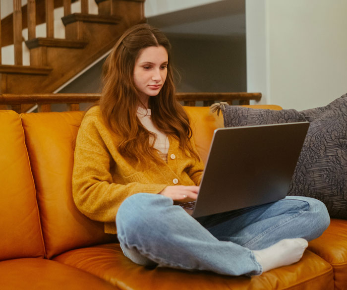 Woman using a laptop on a yellow sofa, exploring internet hacks for easier online life.